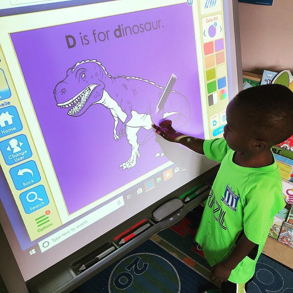 Child interacting with a large screen displaying a dinosaur and text "D is for dinosaur"