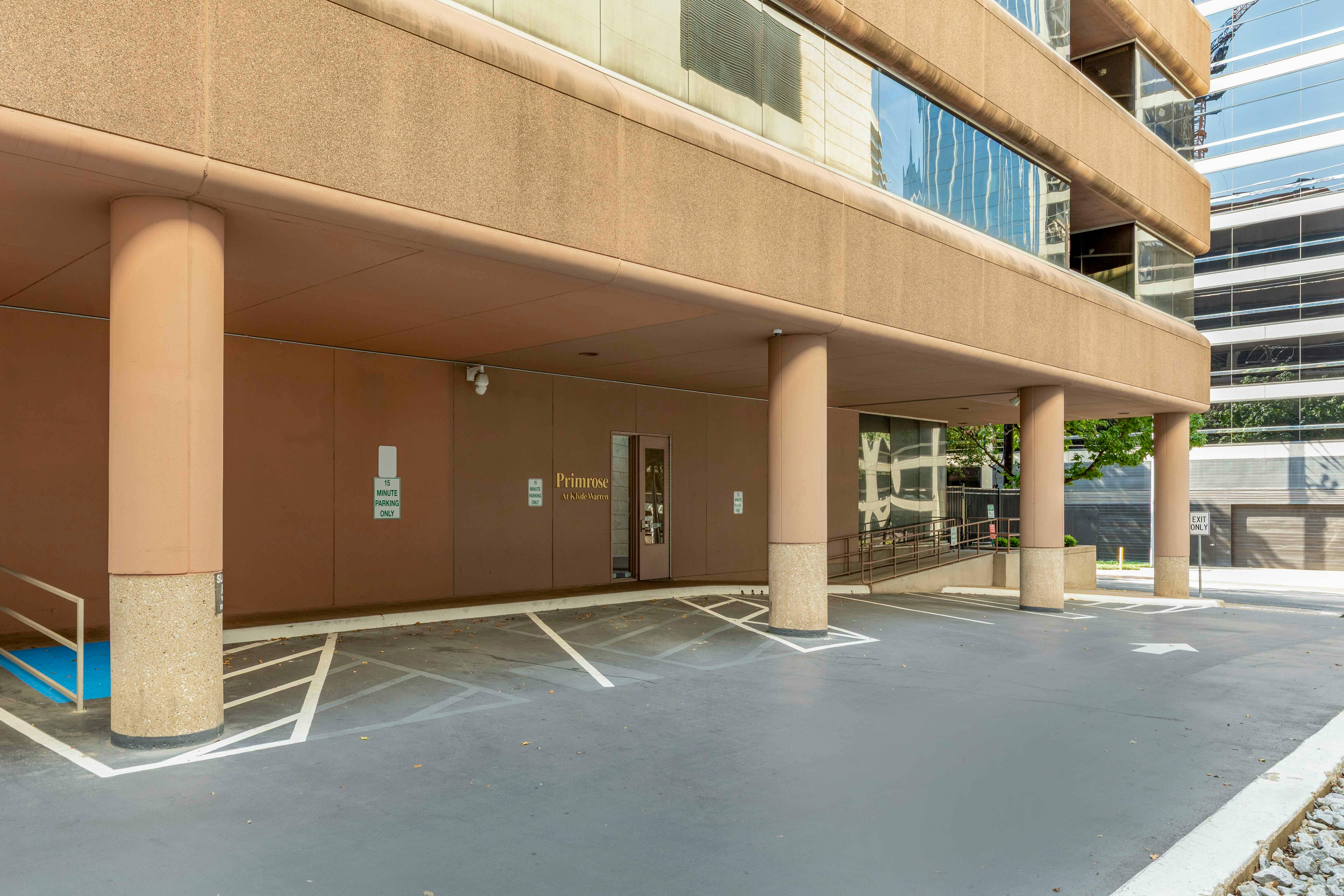 An outdoor parking area under a building with columns and signs for 15-minute parking