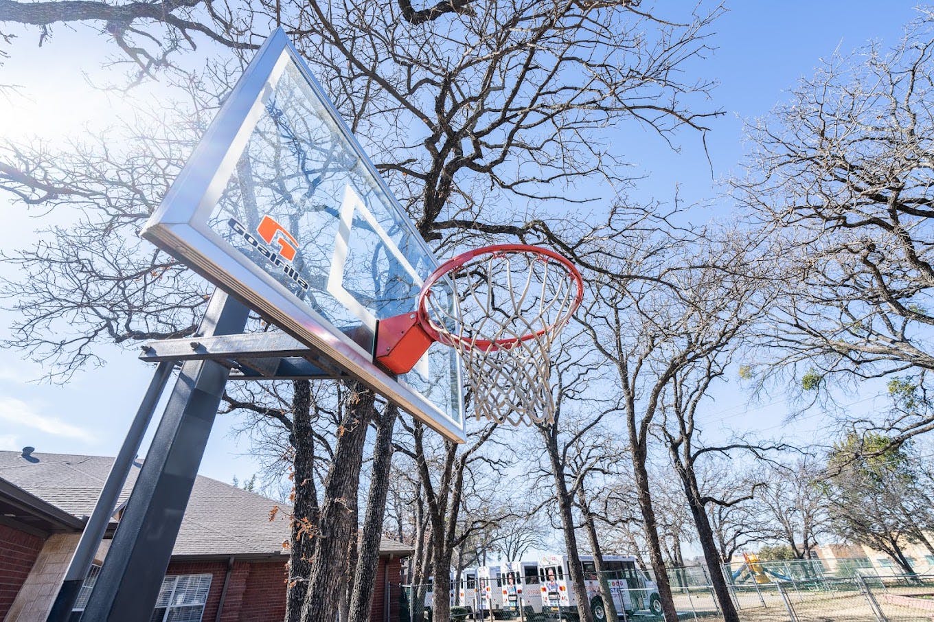 Basketball hoop with a glass backboard outdoors against a backdrop of trees