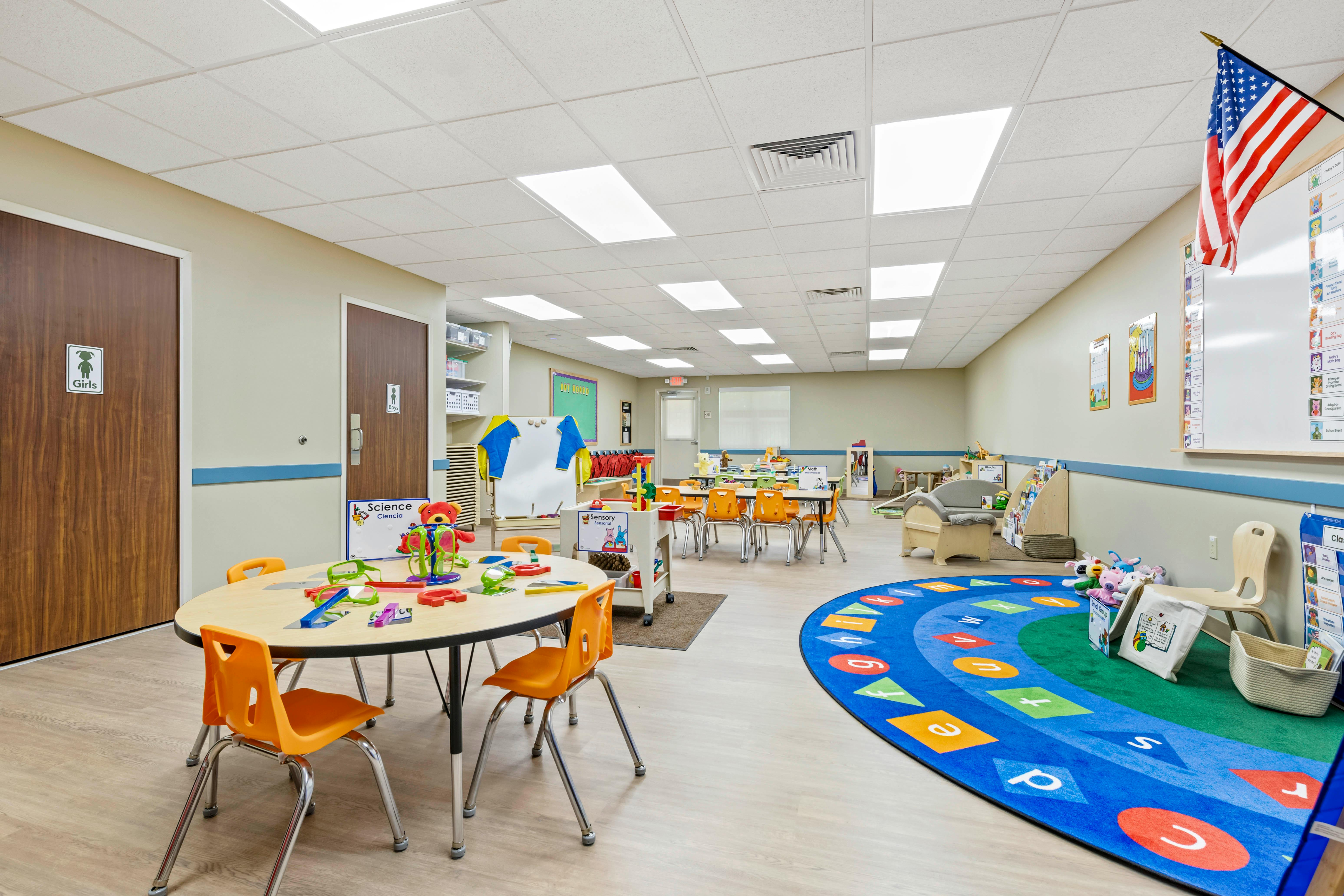 Classroom with tables, chairs, toys, and a colorful alphabet rug