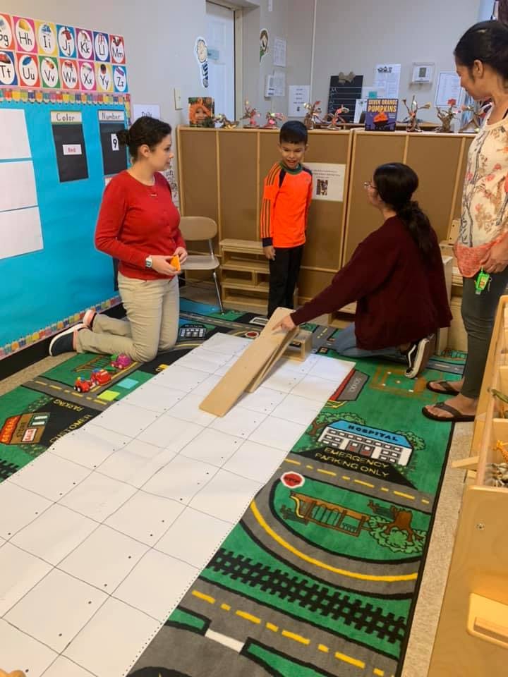 People and a child in a classroom with a ramp and grid on the floor