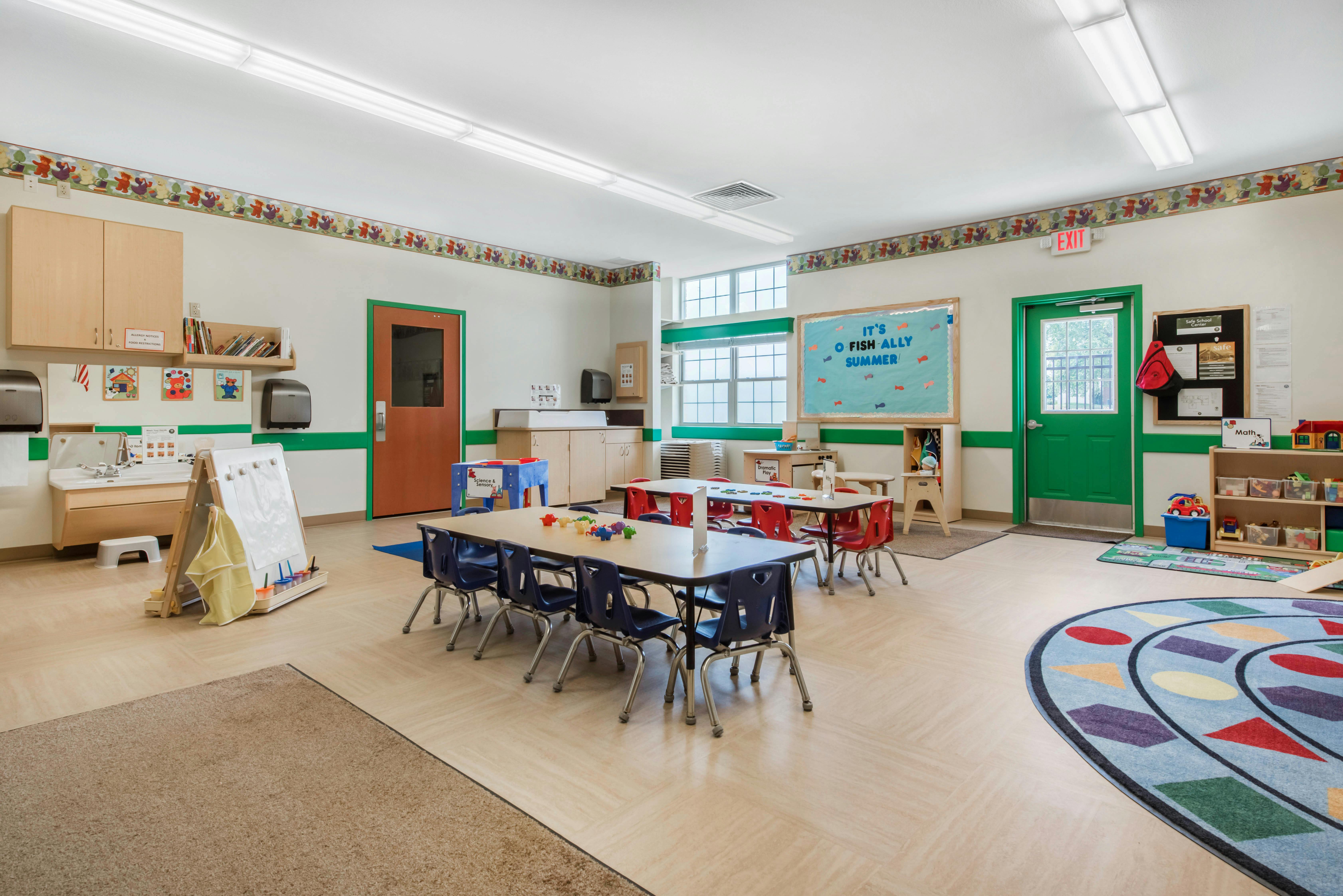 Classroom with child-sized tables and chairs, a sink, and a whiteboard