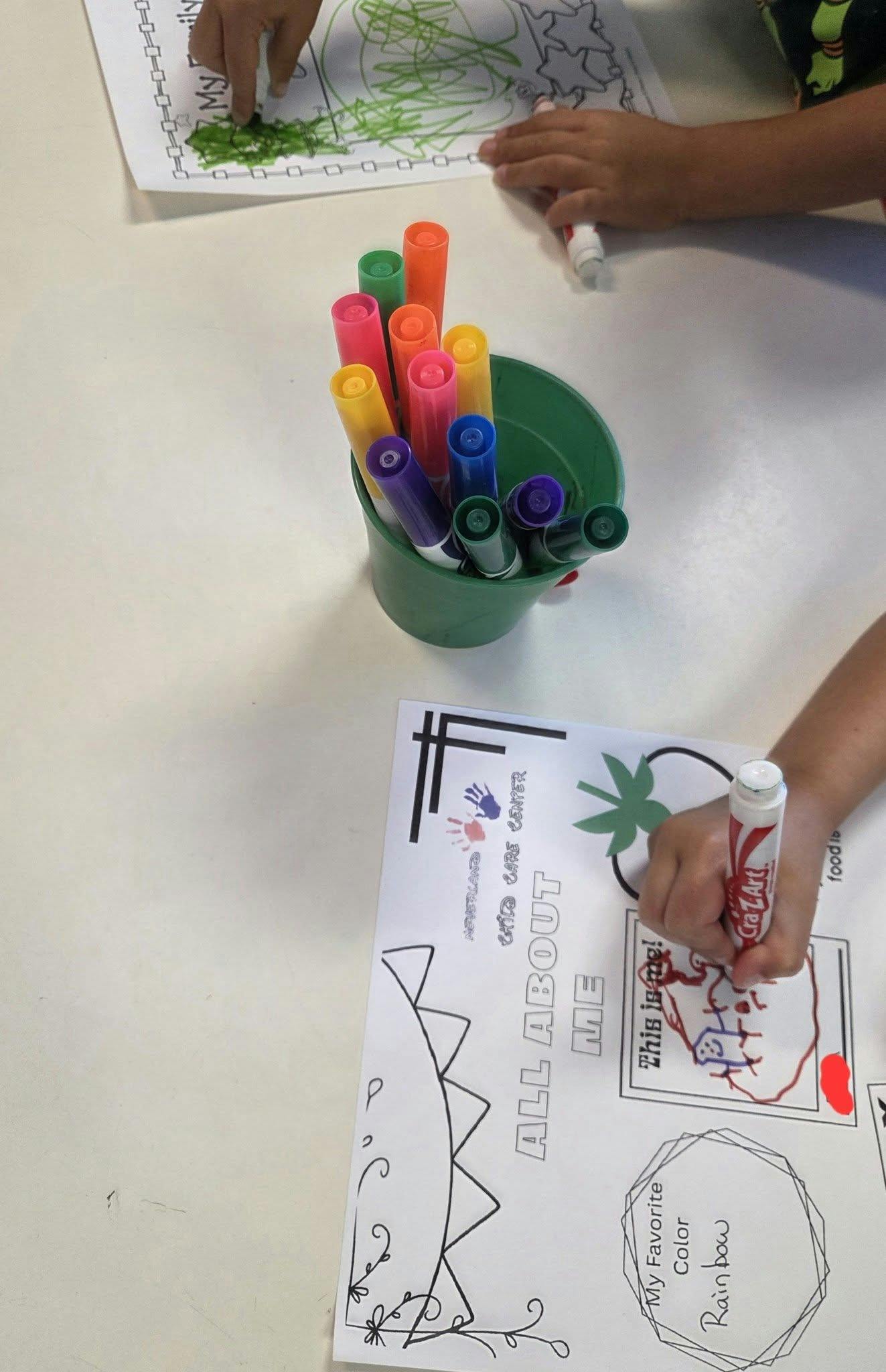 Children's hands coloring papers with markers and a cup of colorful markers