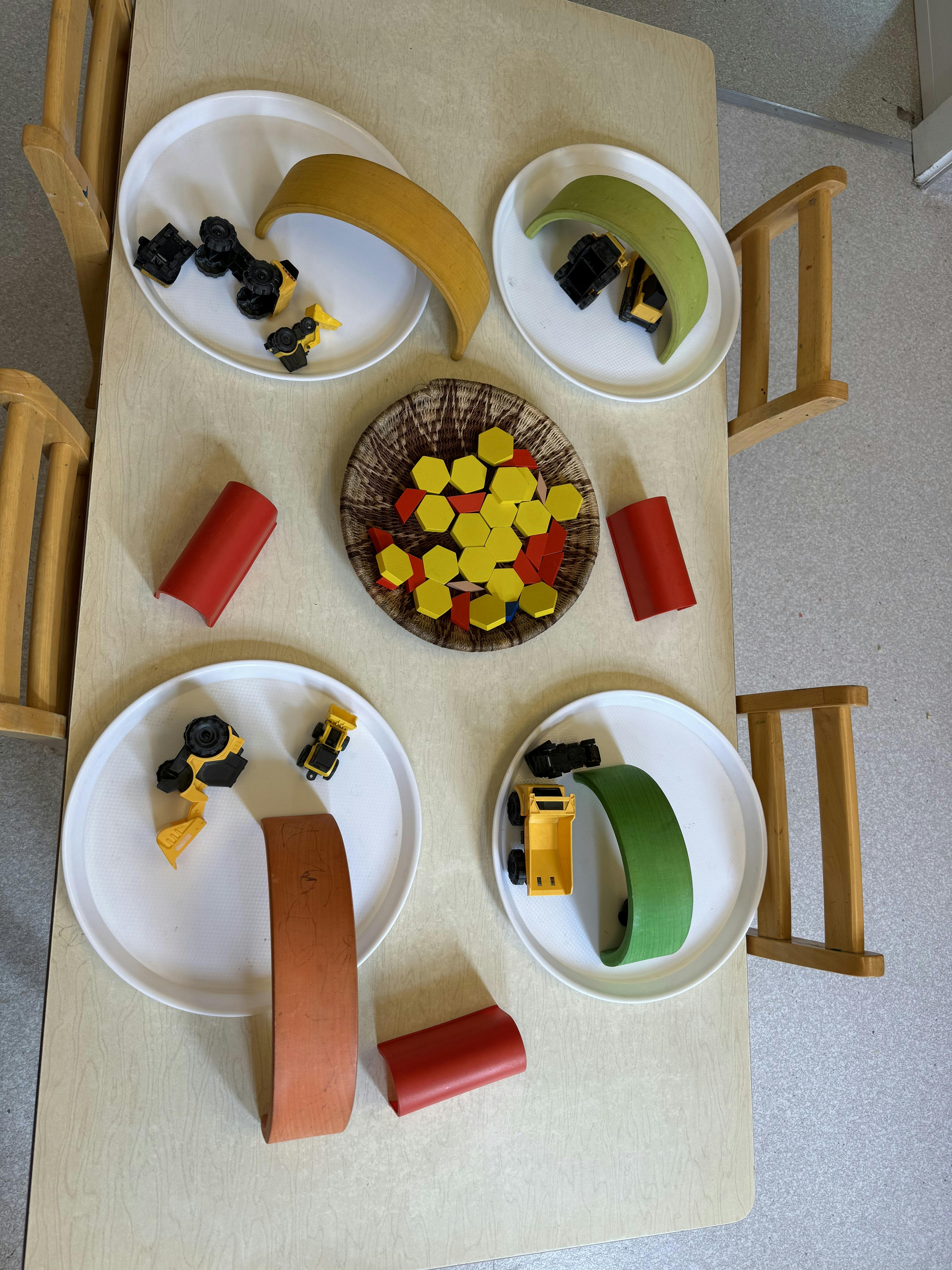 Wooden arch blocks and toy construction vehicles on round trays on a table