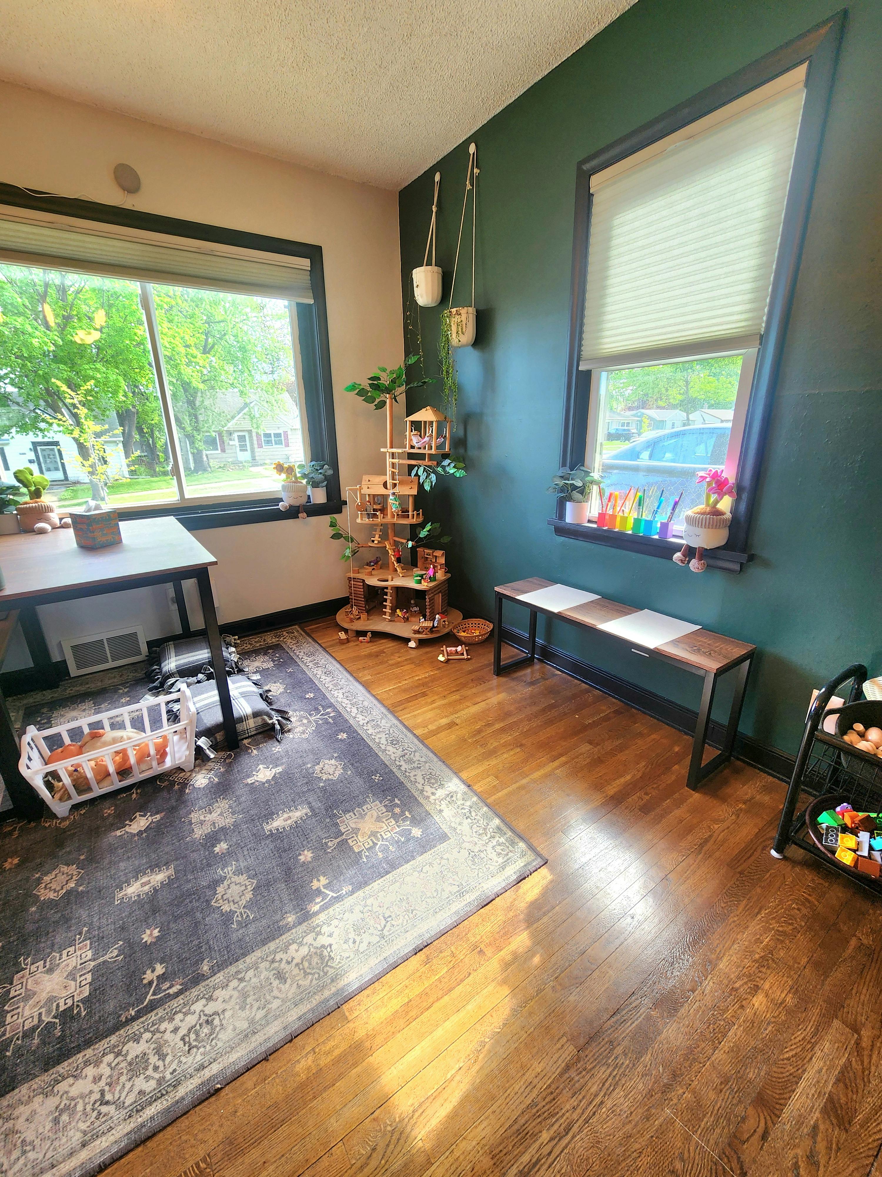 Room with a rug, table, wooden play structure, and bench