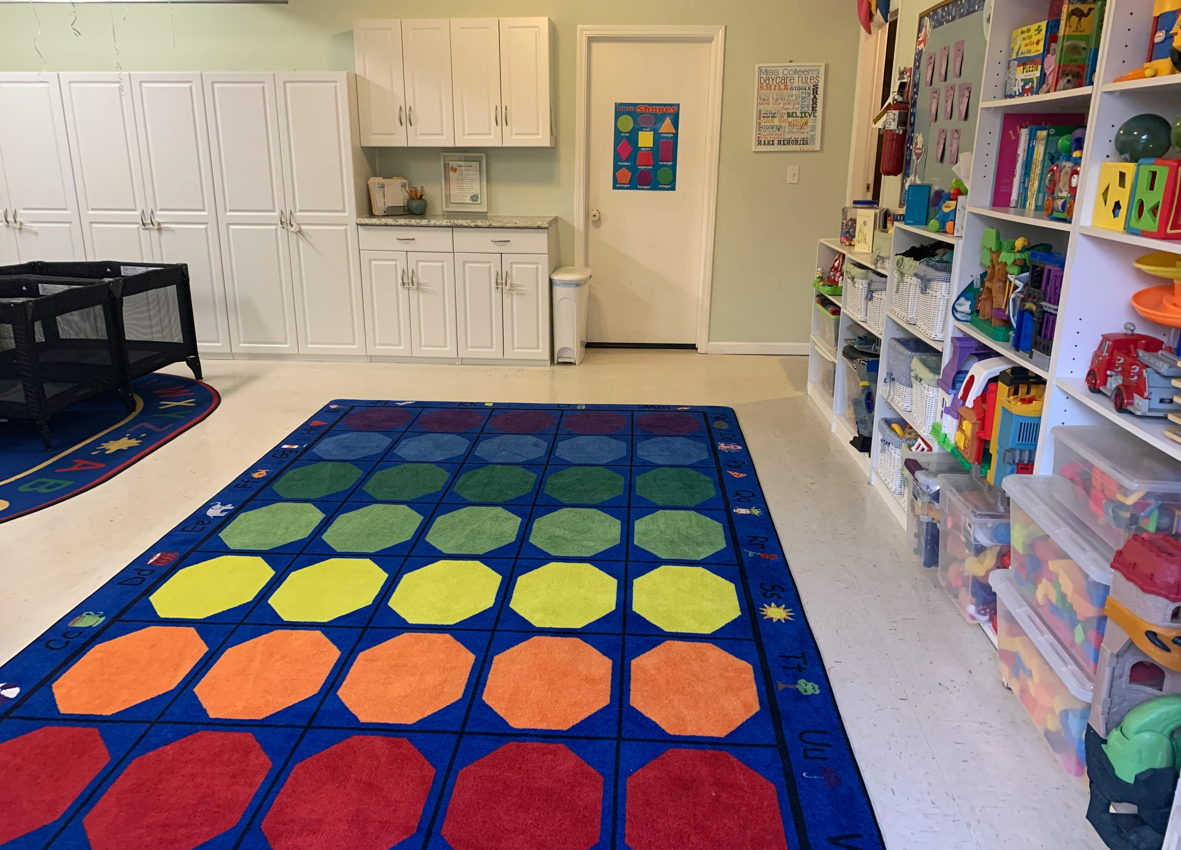 Playroom with colorful rug, shelves of toys, and white cabinets