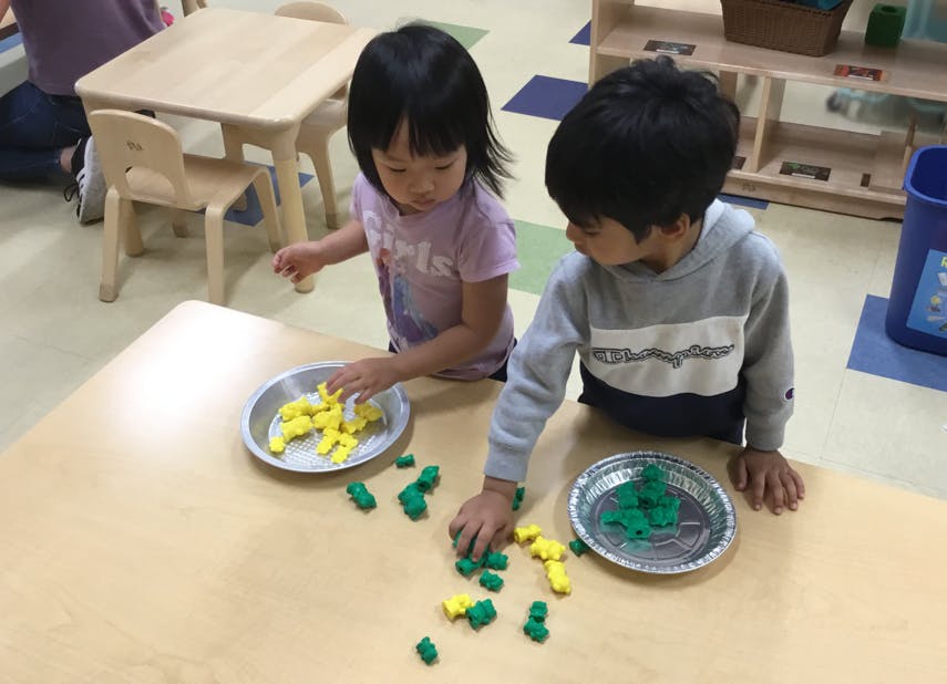 Two children playing with small green and yellow blocks at a table