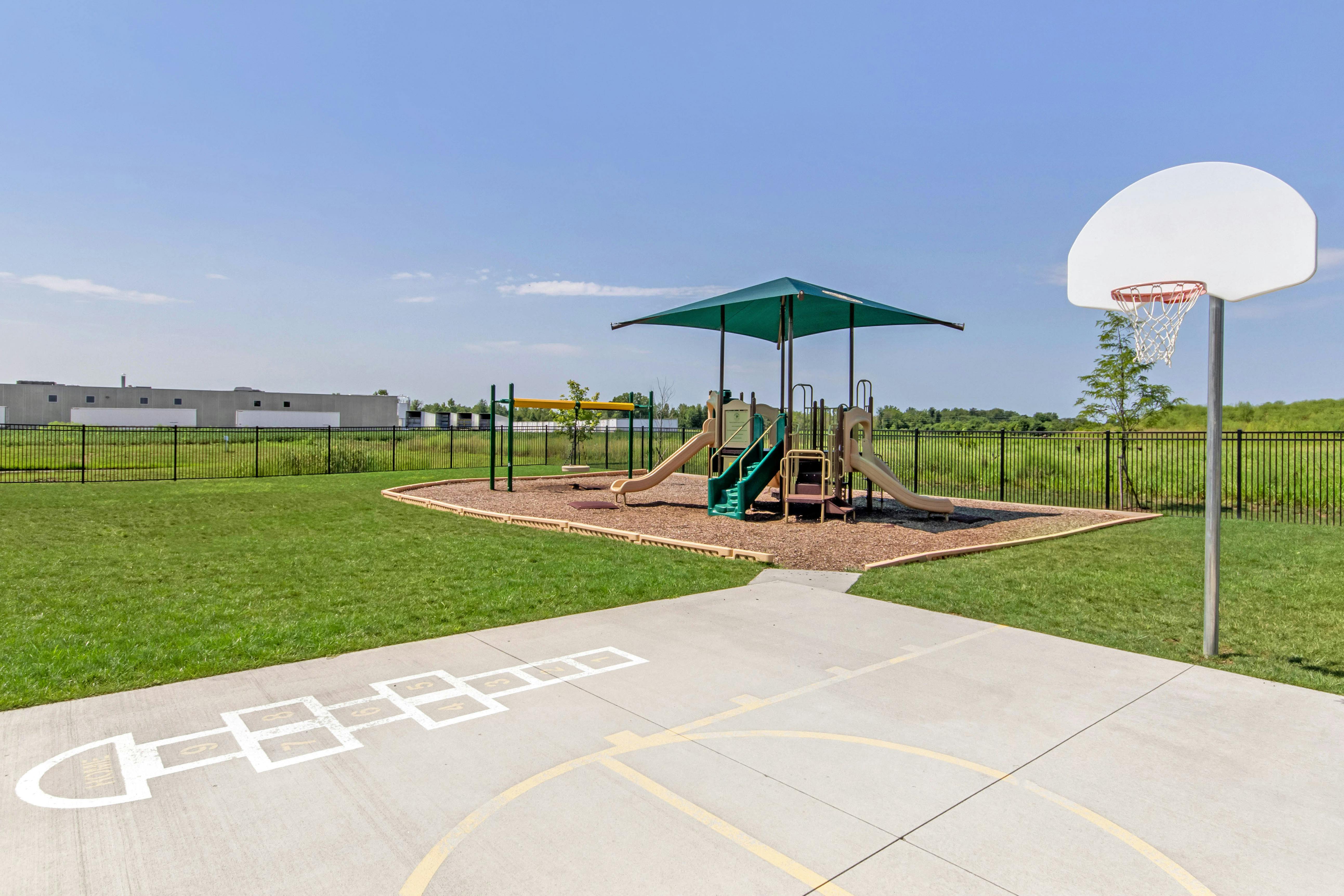 Playground with swings, slides, a basketball hoop, and a hopscotch court