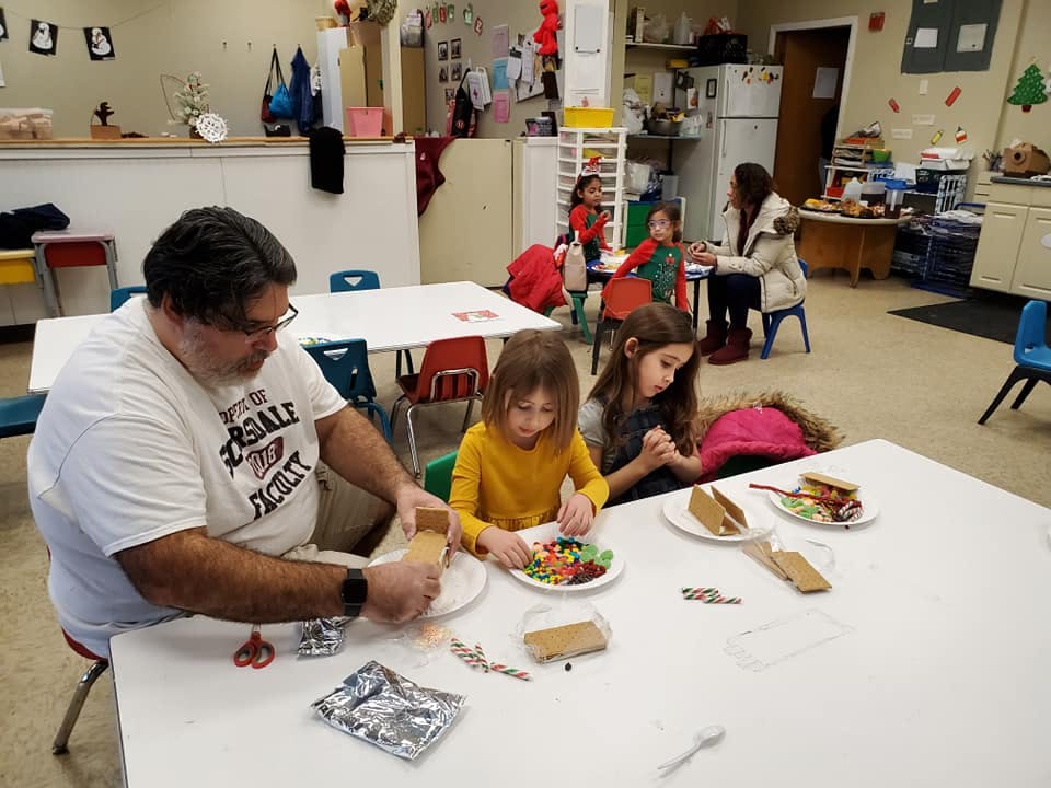 Person and two children decorating gingerbread houses at a table