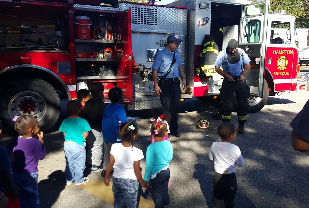 Children watching firefighters near a fire truck