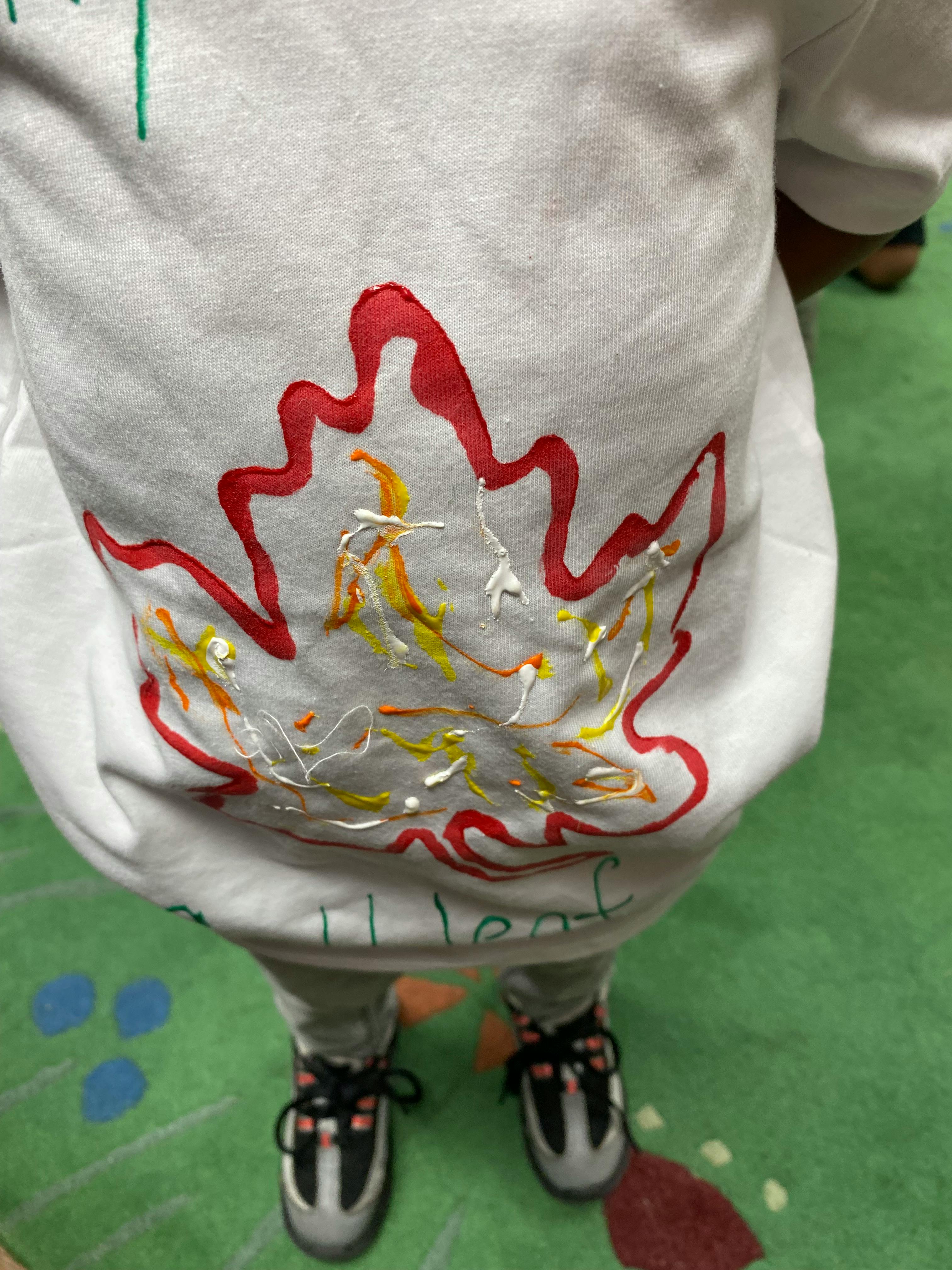 Child wearing a white shirt with a red and yellow leaf design