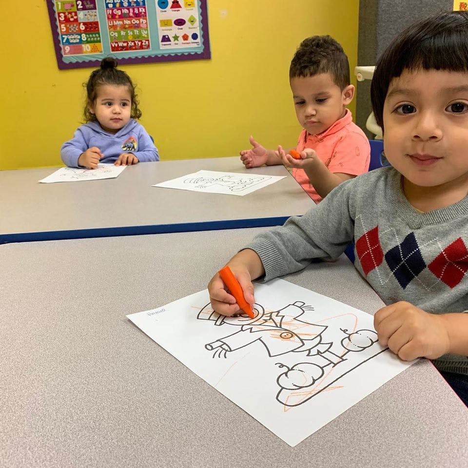 Three children coloring at a table in a classroom