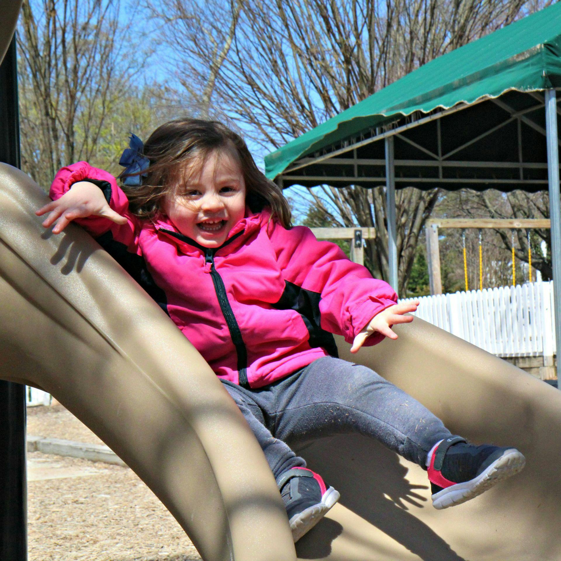 Child in a pink jacket going down a slide