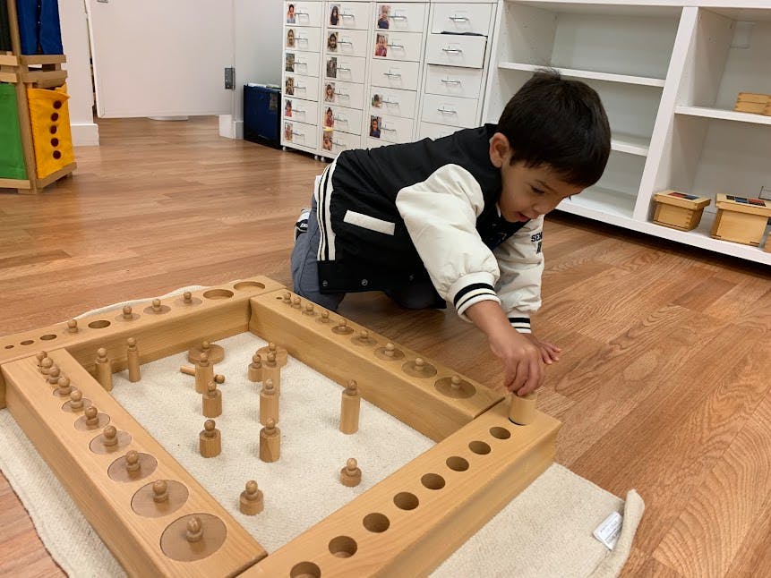 Child playing with a wooden peg board puzzle on the floor