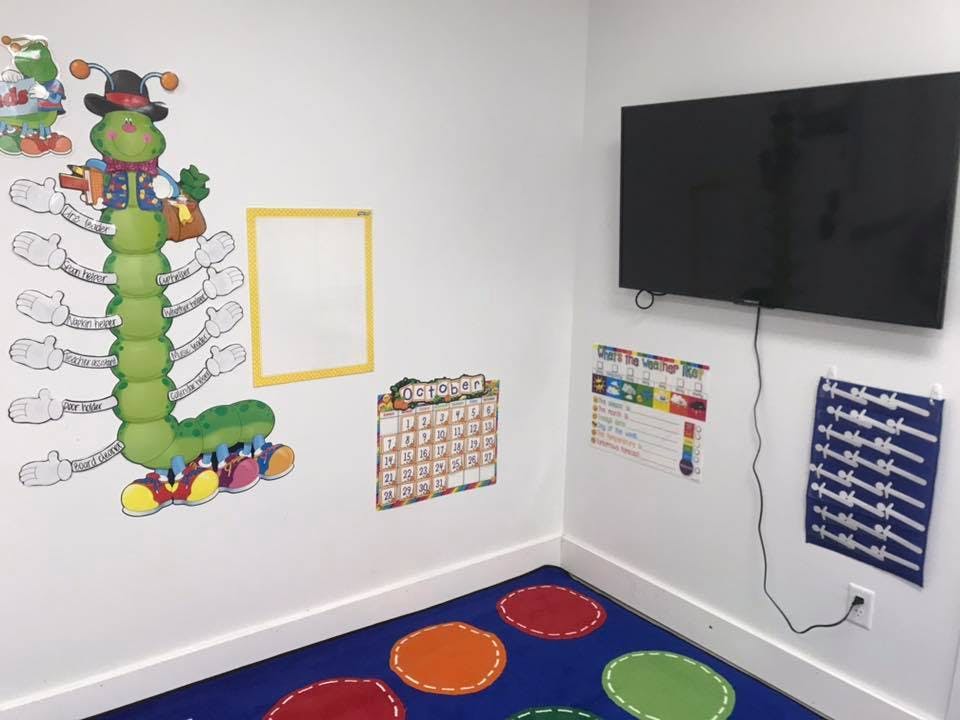 Classroom corner with a large caterpillar wall decal, calendar, and TV