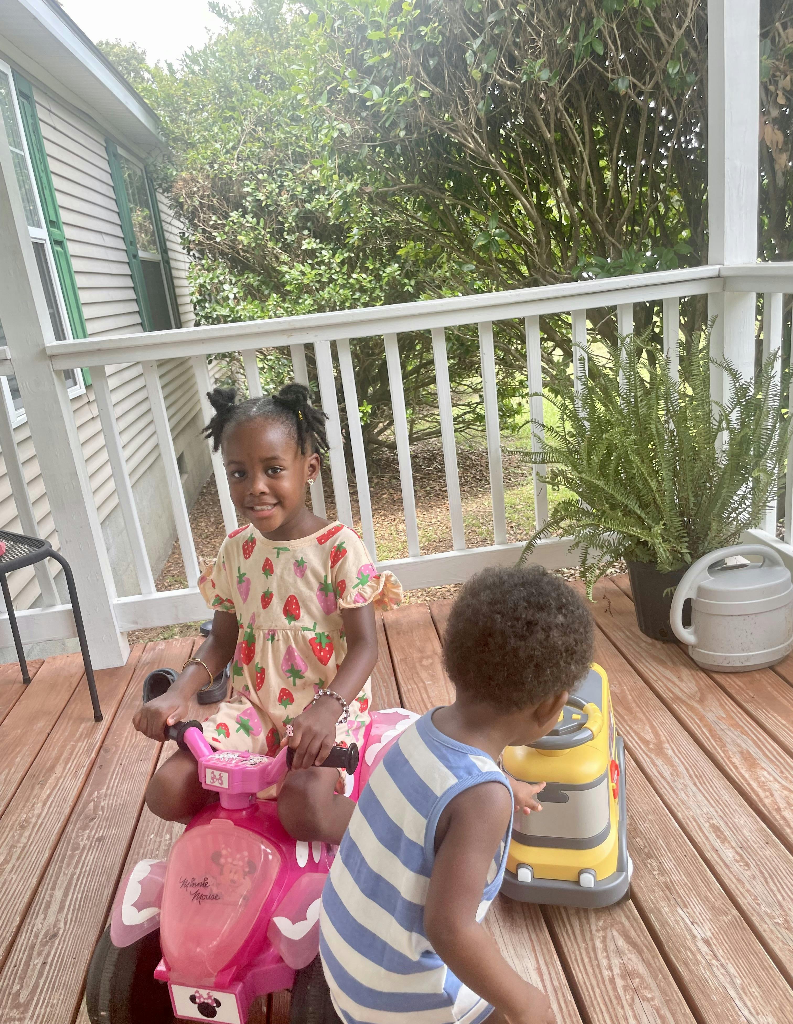 Two children playing on ride-on toys on a wooden porch