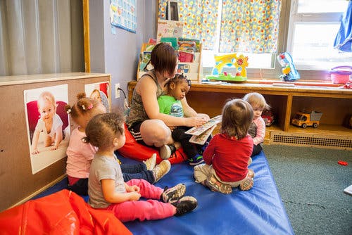 Adult reading a book to several children in a classroom
