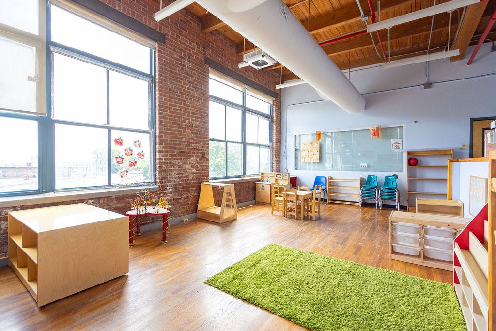Empty classroom with large windows, brick walls, and small tables and chairs