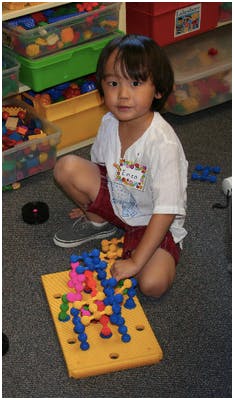 Child kneeling on floor playing with colorful construction toy