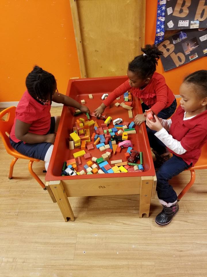 Three children playing with building blocks at a table