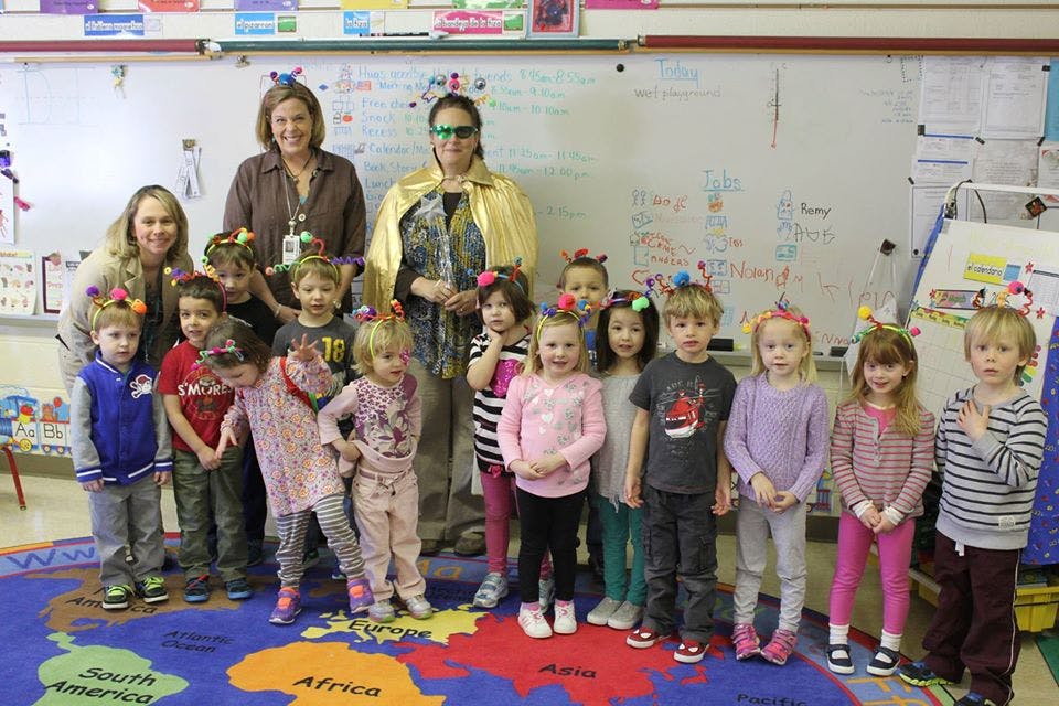 Two adults and a group of children standing in a classroom