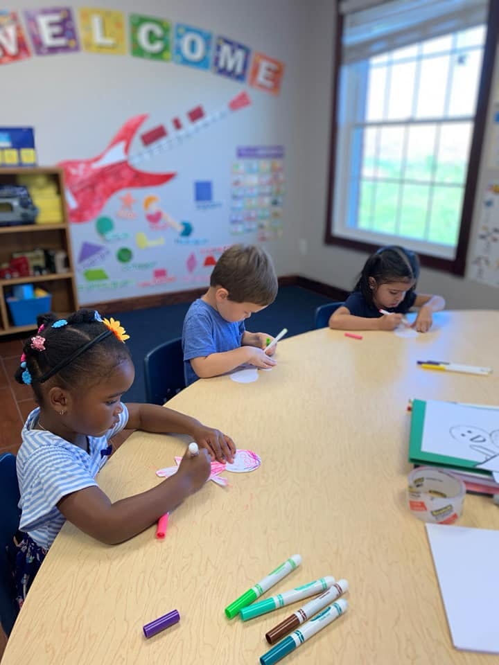 Three children coloring at a table in a classroom