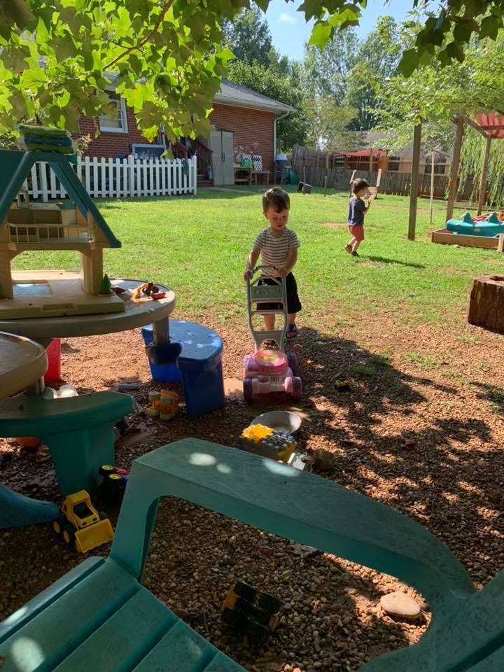 Child pushing a toy lawnmower in a yard