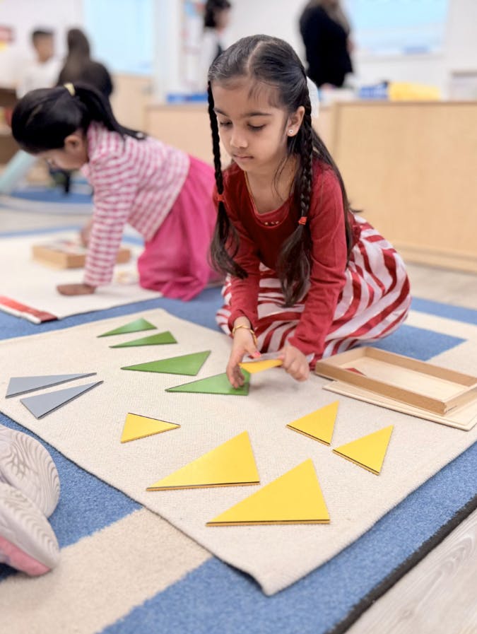 Child playing with triangle shapes on a rug in a classroom