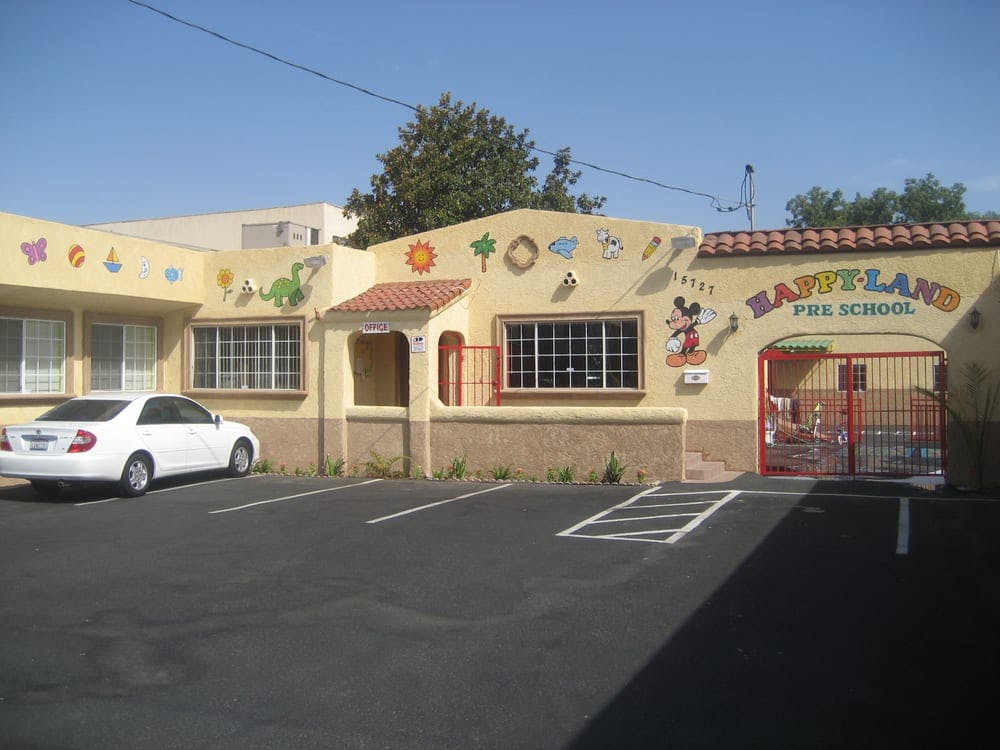 Preschool building with "HAPPY-LAND PRE-SCHOOL" sign and a white car in the parking lot