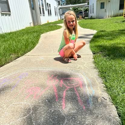 Child crouching on a sidewalk next to chalk drawings