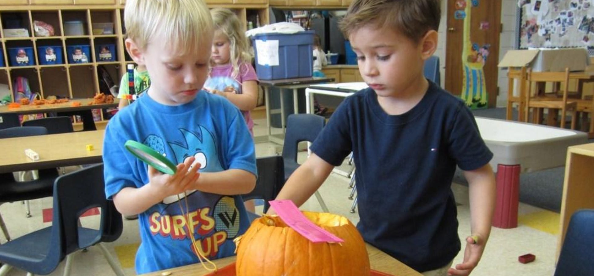 Two children carving a pumpkin in a classroom