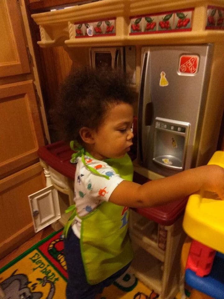 Child in a green bib playing with a toy kitchen set
