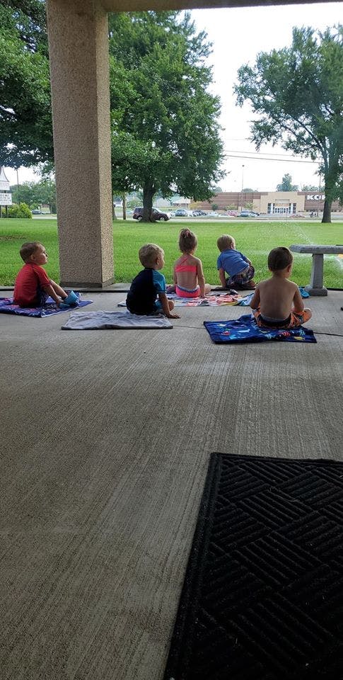 Five children sitting on towels on a concrete patio, facing away