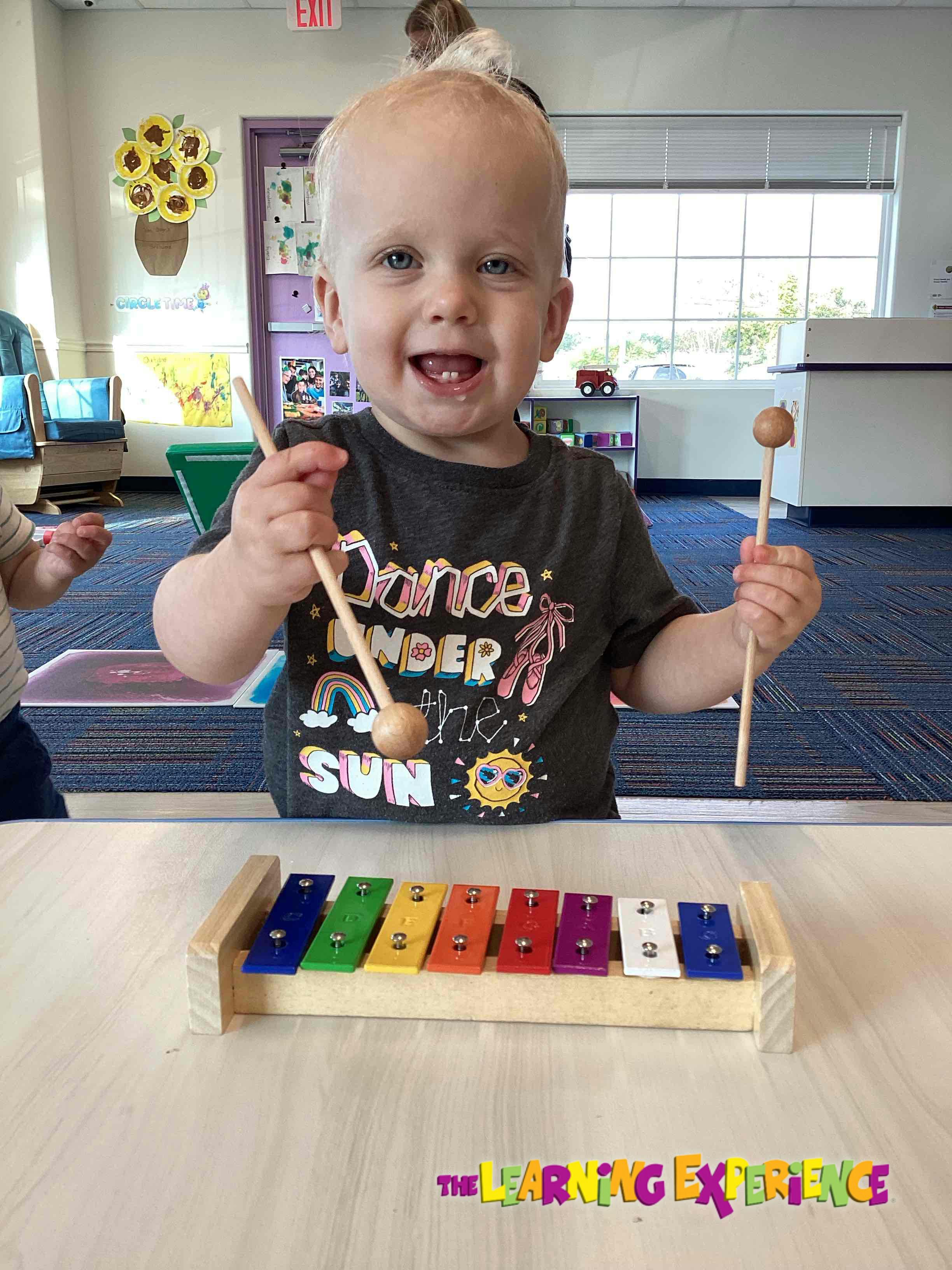 Child holding mallets over a colorful xylophone
