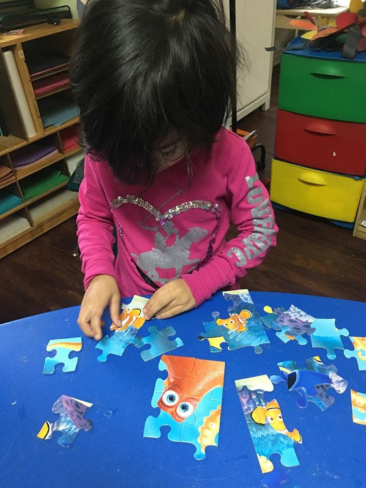 Child assembling a puzzle on a blue table