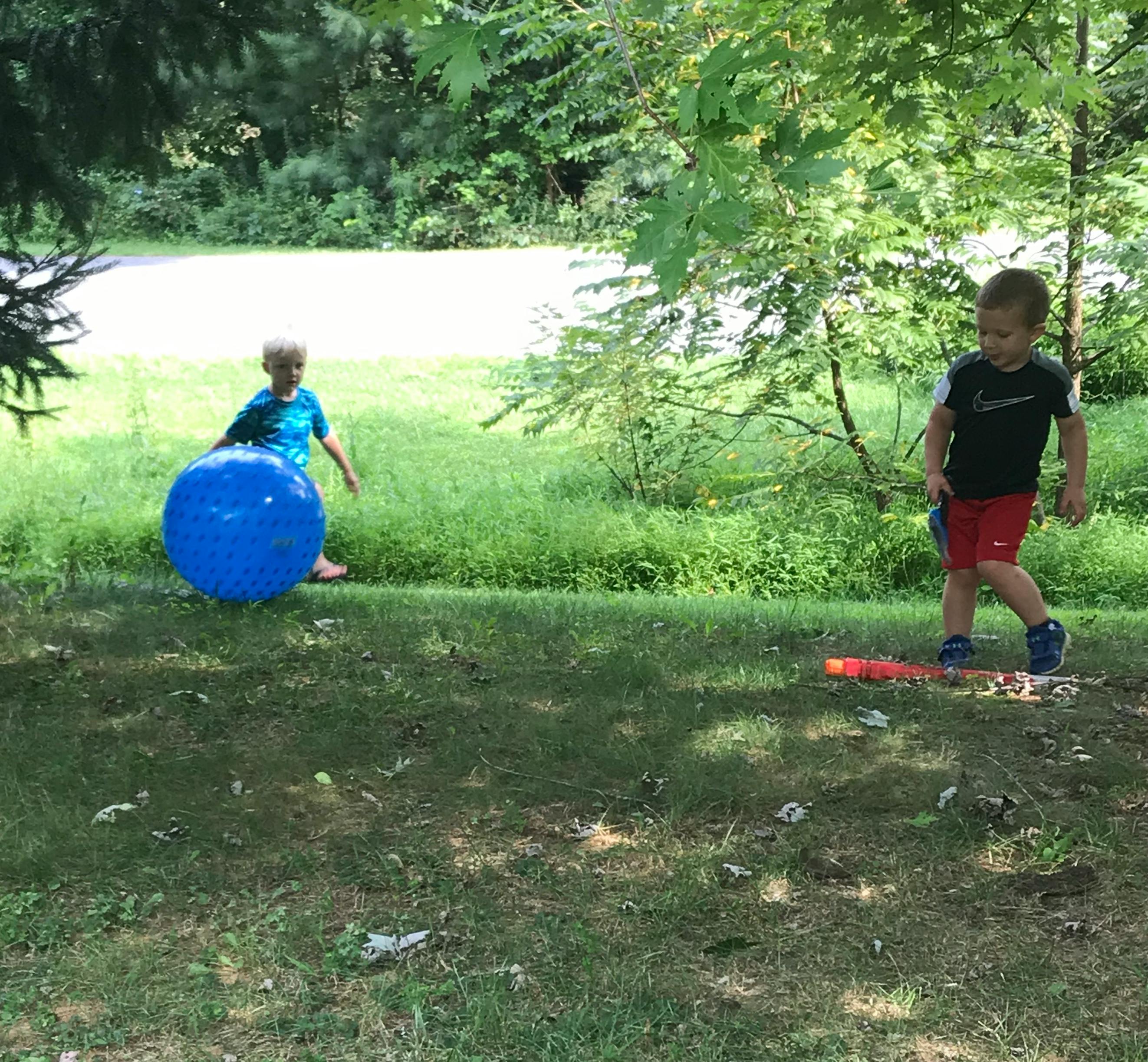 Two children playing with a large blue ball and a toy bat in a grassy area