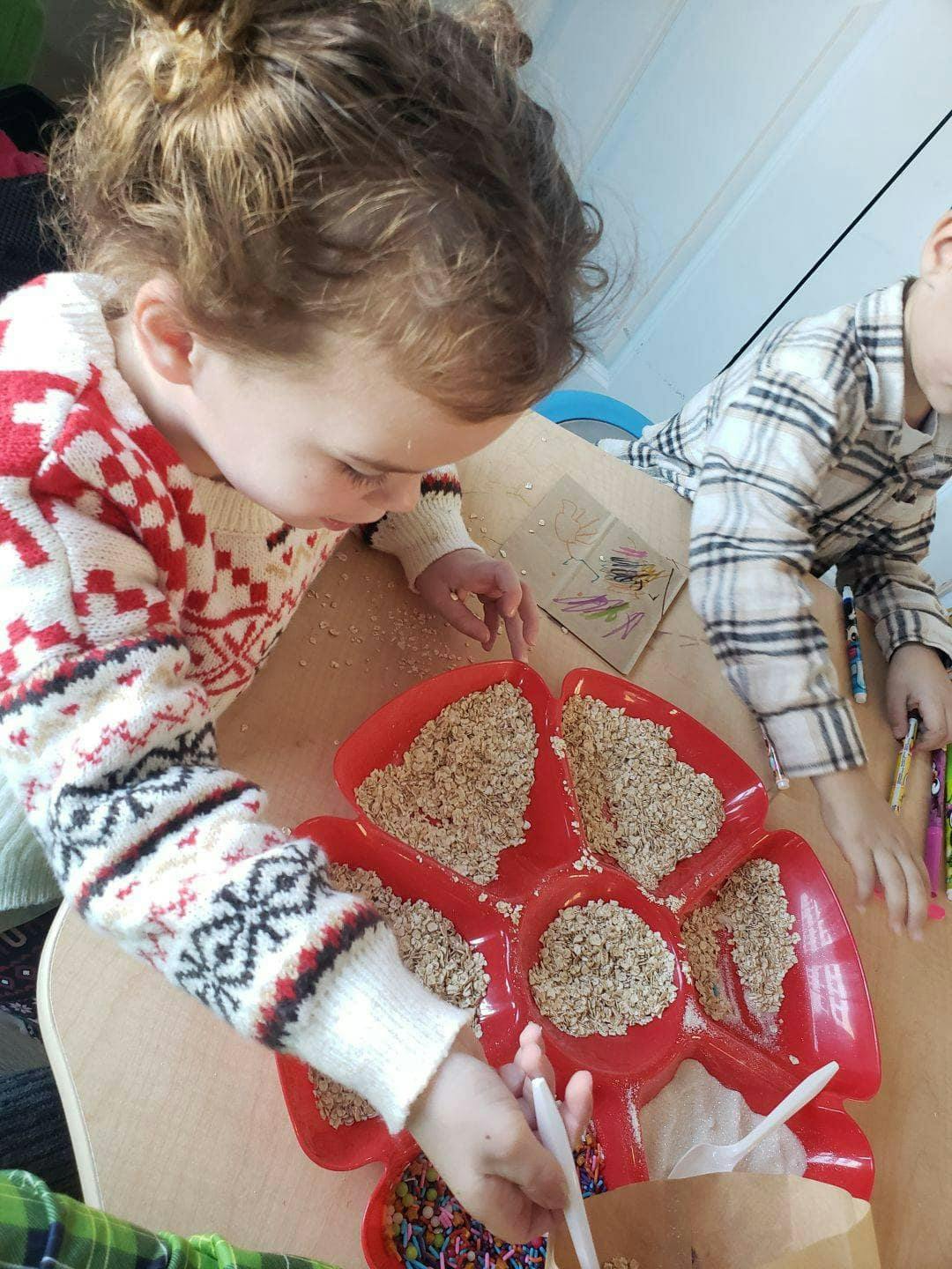 Child looking at a red tray with compartments filled with grains