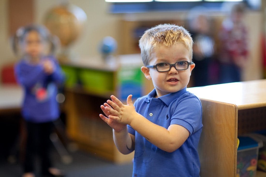 Child in glasses clapping hands in a classroom