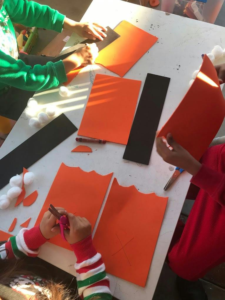 Children cutting and arranging orange and black paper on a table