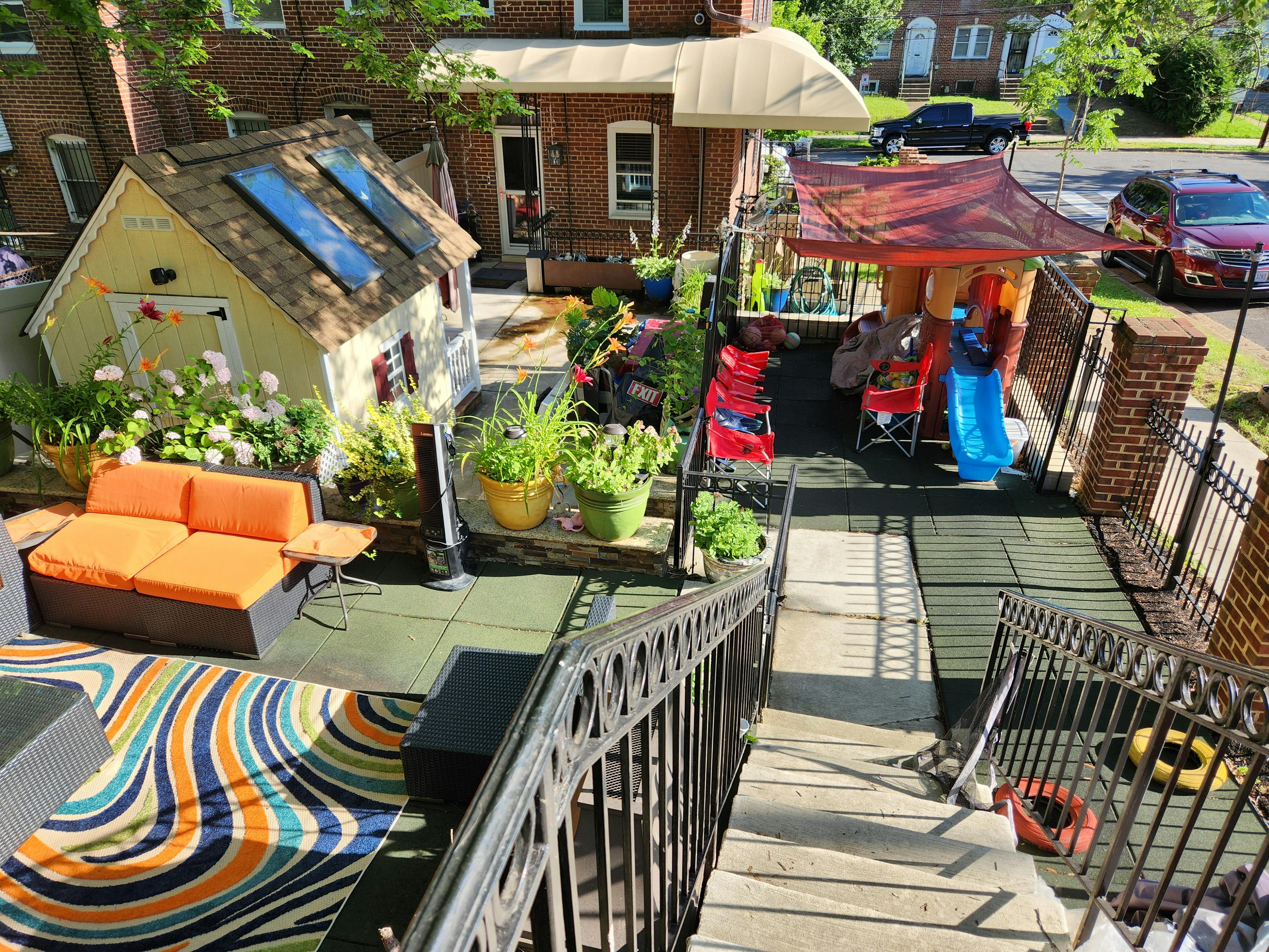 Outdoor patio with orange sofa, colorful rug, and play area with slide