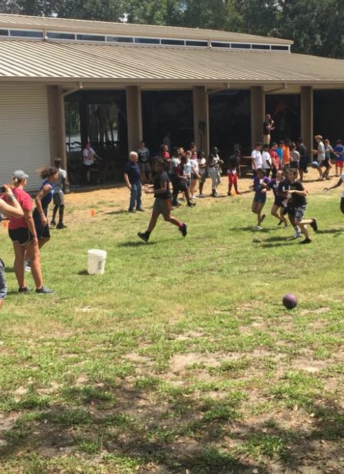 People playing kickball on a grassy field near a building