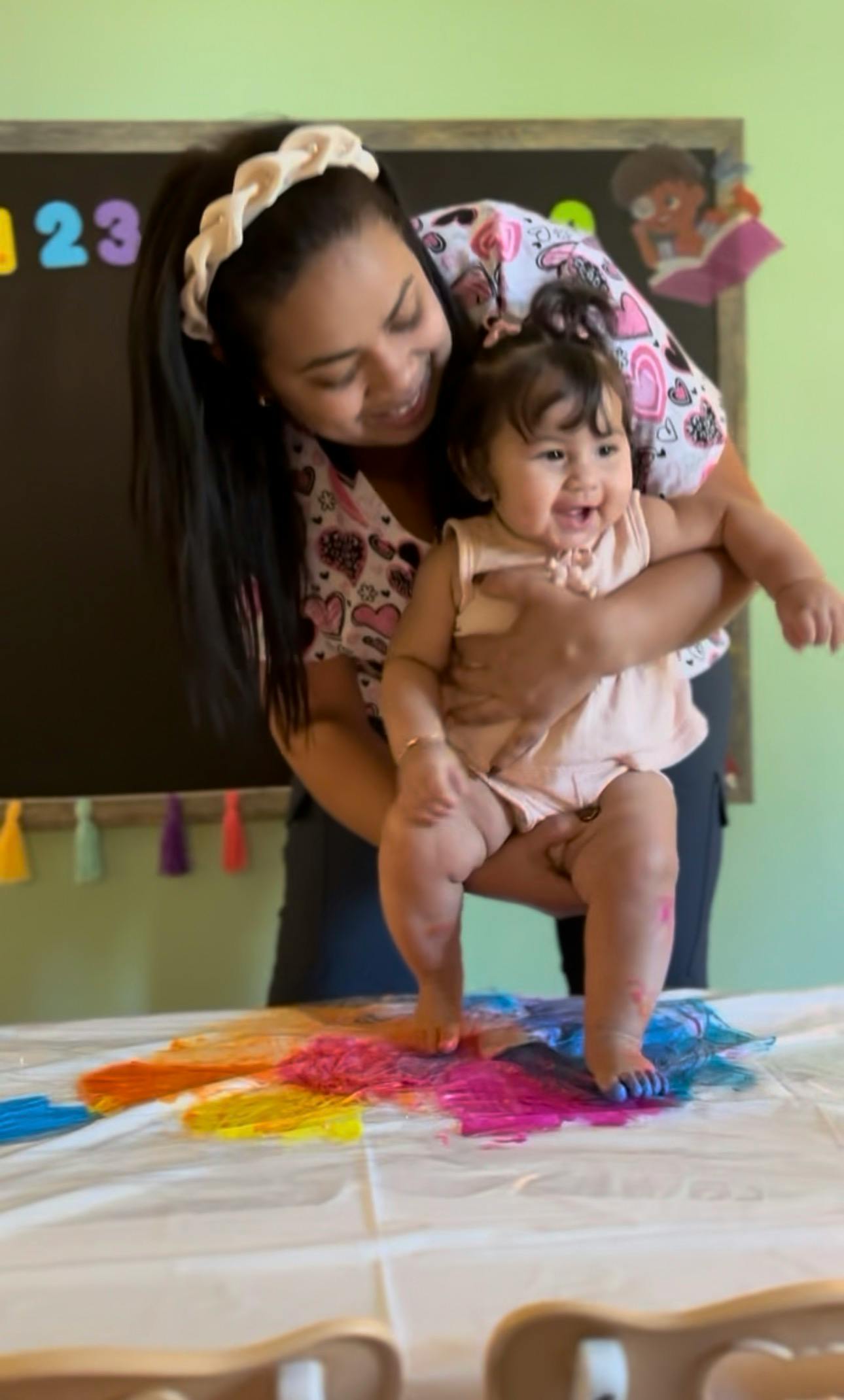 Person holding a child standing on a table covered in colorful paint
