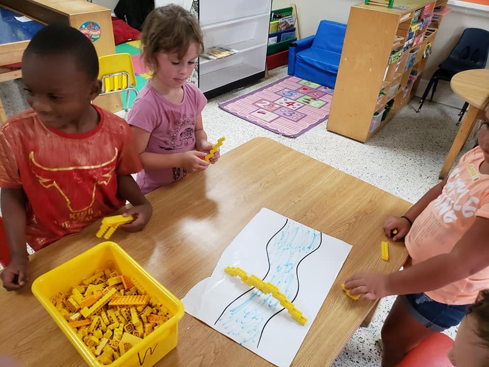 Three children at a table with yellow building blocks and a drawing