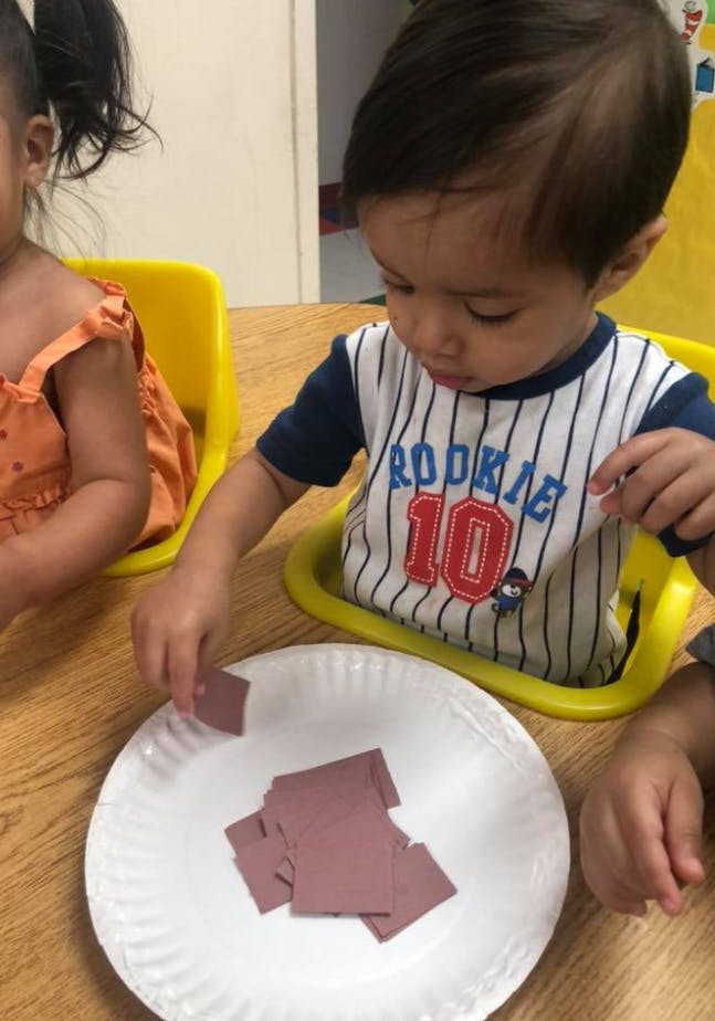 Child in a high chair playing with paper squares on a plate