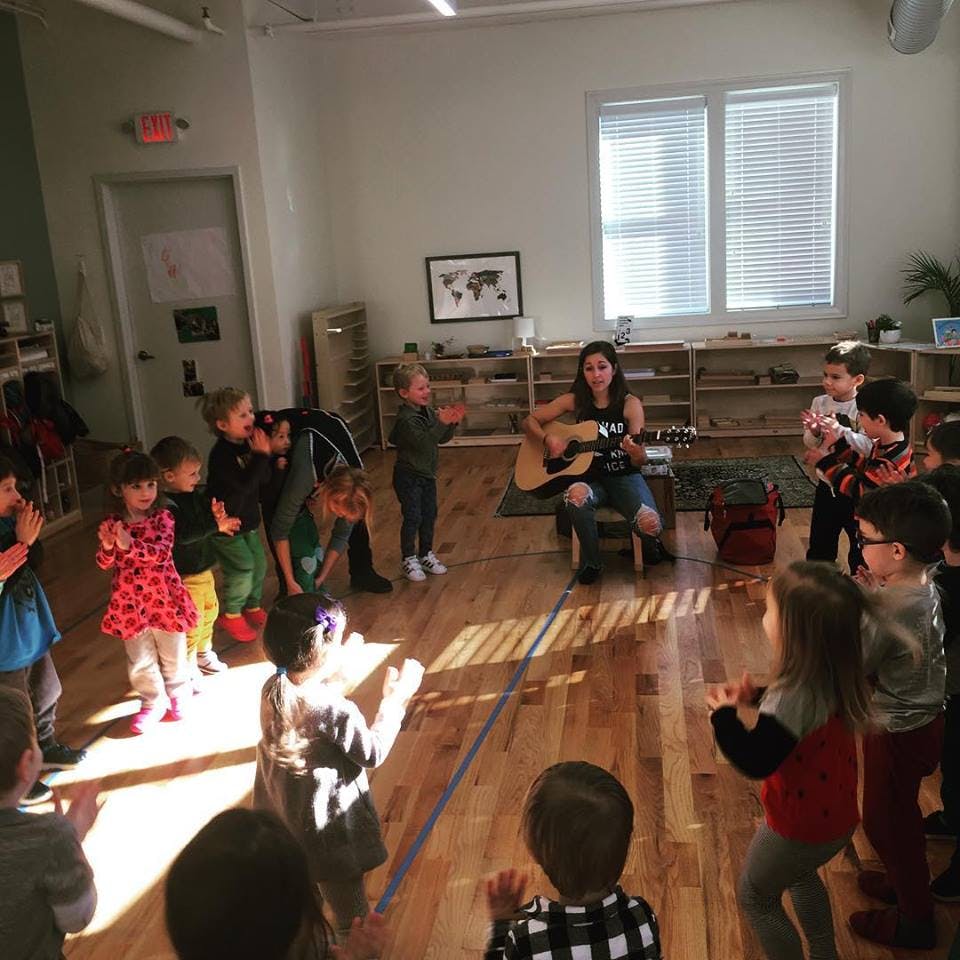 Person playing guitar for a group of children in a classroom