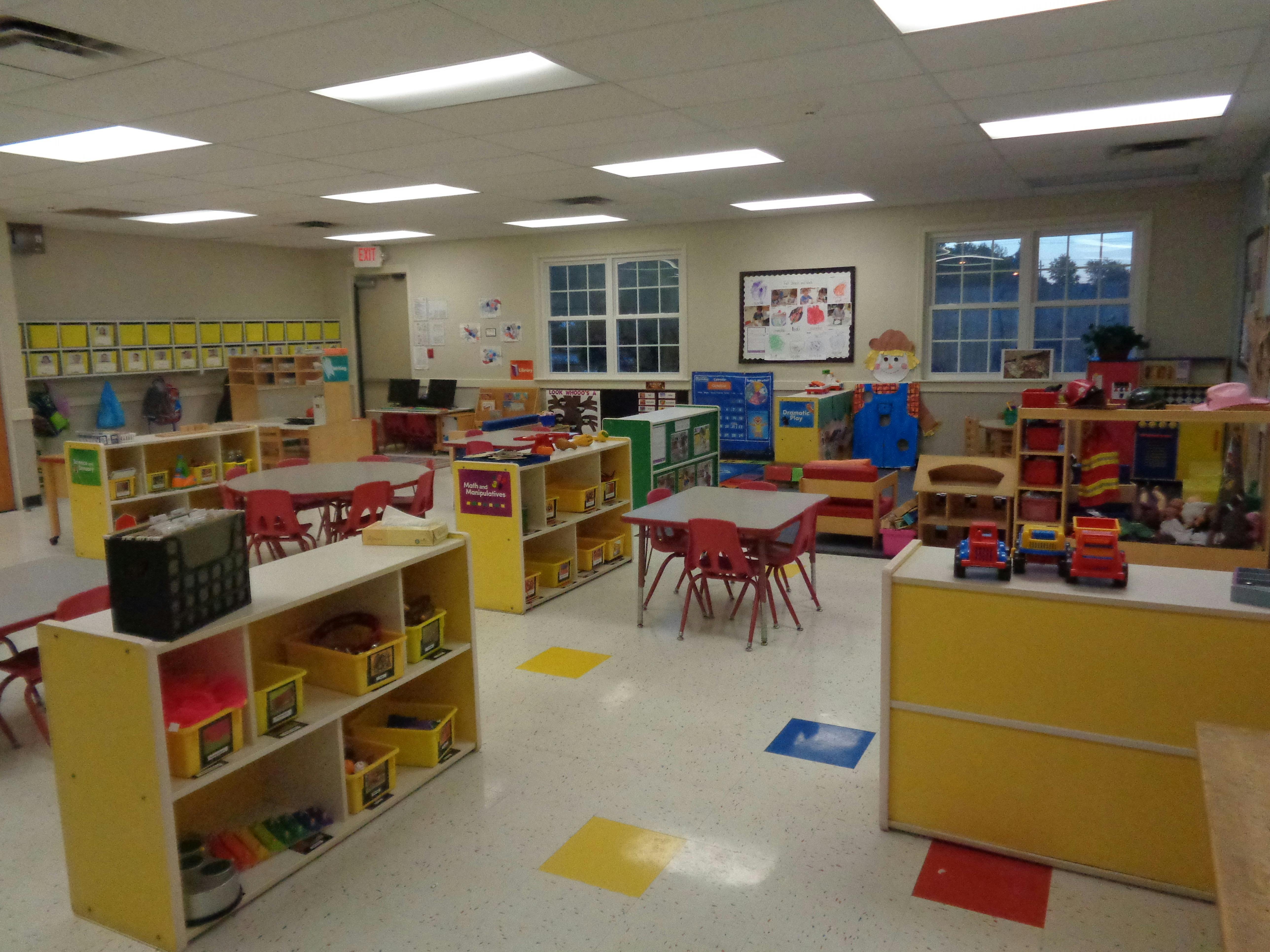 Classroom with small red tables, chairs, and shelves filled with toys and supplies