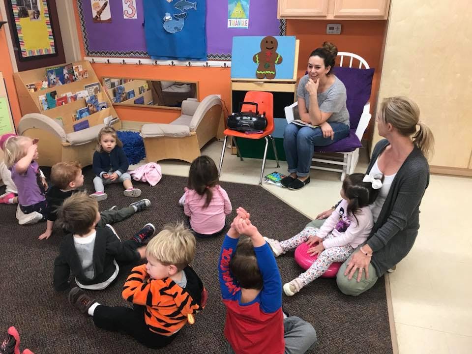 Two people with a group of children sitting on the floor in a classroom