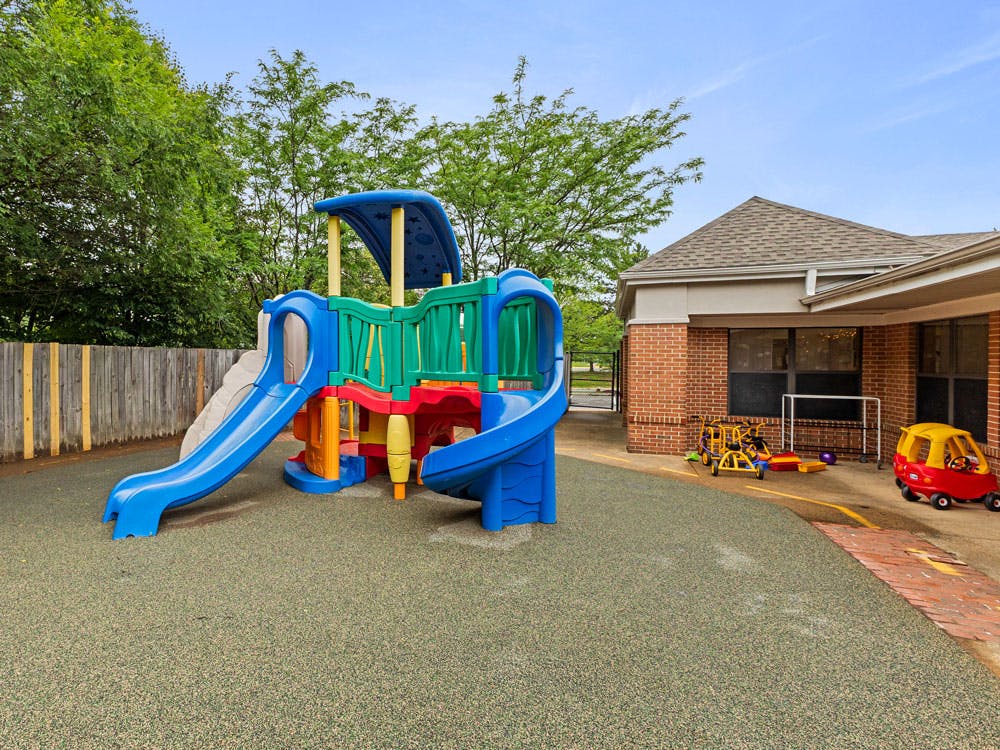 Colorful playground structure with slides on a soft green ground next to a brick building