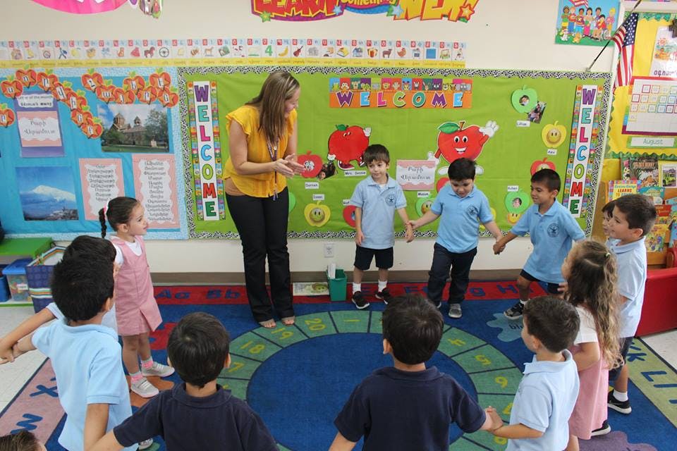 Adult and children holding hands in a circle in a classroom