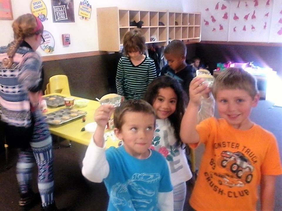 Children holding up cupcakes in a classroom